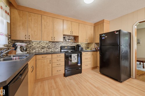 Kitchen featuring light wood-finish cabinetry, dark countertops, and a mosaic tile backsplash - 11414 88 Street Nw, Edmonton, AB 