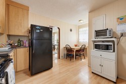 Kitchen featuring light wood-finish flooring, wood cabinetry, a black refrigerator, and light-toned paneled walls - 