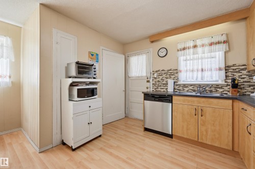 Kitchen featuring wood-finish flooring, light-toned cabinetry, stainless steel dishwasher, dark countertops, and a mosaic tile backsplash - 11414 88 Street Nw, Edmonton, AB 