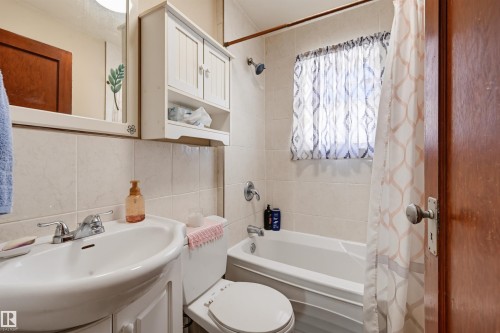 Full bathroom featuring a white vanity with a ceramic sink, a mirrored medicine cabinet, and a bathtub with a shower - 11414 88 Street Nw, Edmonton, AB 