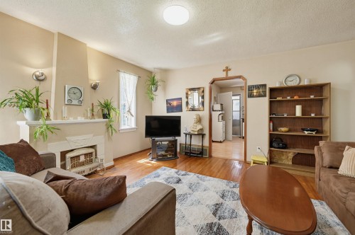 Living area featuring wood-finish flooring, a decorative fireplace with a mantel, recessed wall sconces, and a built-in shelving unit - 11414 88 Street Nw, Edmonton, AB 