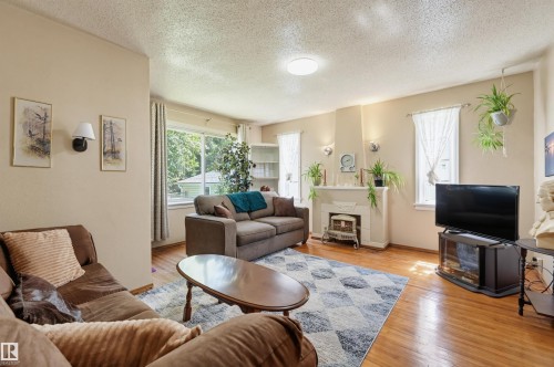 Living area featuring wood-finish flooring, a decorative fireplace with a mantel, and multiple windows for natural light - 11414 88 Street Nw, Edmonton, AB 
