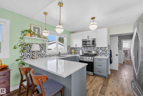 Kitchen featuring an eat-at peninsula with a white countertop, patterned tile backsplash, stainless steel appliances, and two pendant light fixtures - 14128 73 Street, Edmonton, AB 