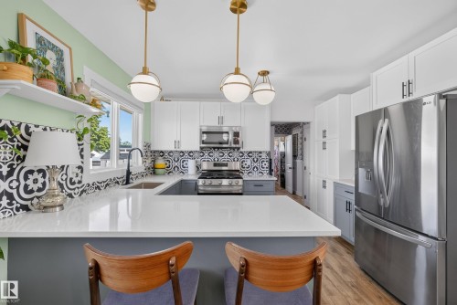 Modern kitchen featuring white cabinetry, stainless steel appliances, a gas range, and a patterned tile backsplash - 14128 73 Street, Edmonton, AB 