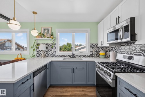 Kitchen featuring light green walls, a black and white patterned tile backsplash, white countertops, and wood-finish flooring - 14128 73 Street, Edmonton, AB 
