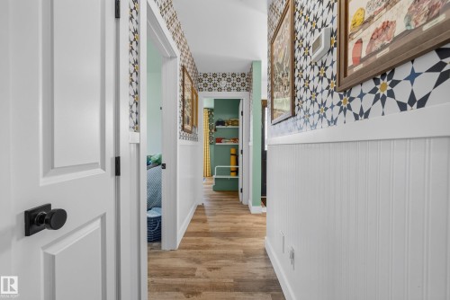 Hallway featuring wood-finish flooring and patterned wallpaper above white wainscoting - 14128 73 Street, Edmonton, AB 