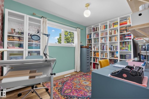 Dedicated room featuring extensive built-in shelving, glass-front cabinetry, wood-finish flooring, and a large window - 14128 73 Street, Edmonton, AB 