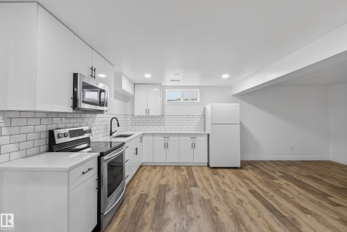 U-shaped kitchen featuring white cabinetry, subway tile backsplash, stainless steel appliances, and wood-finish flooring - 14128 73 Street, Edmonton, AB 