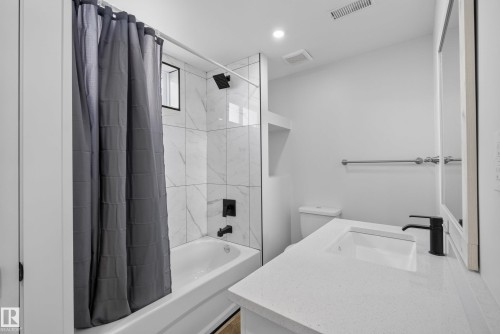 Modern bathroom featuring a white vanity with an integrated sink, black single-handle faucet, and white countertop - 14128 73 Street, Edmonton, AB 