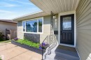 Entryway featuring a black panel door with decorative glass, light green siding, white trim windows, and a raised garden bed with a black lattice accent - 14128 73 Street, Edmonton, AB 
