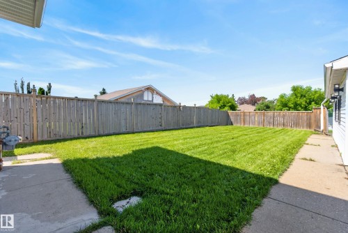 Spacious backyard featuring a manicured lawn, full-height privacy fencing, and concrete pathways - 14128 73 Street, Edmonton, AB 