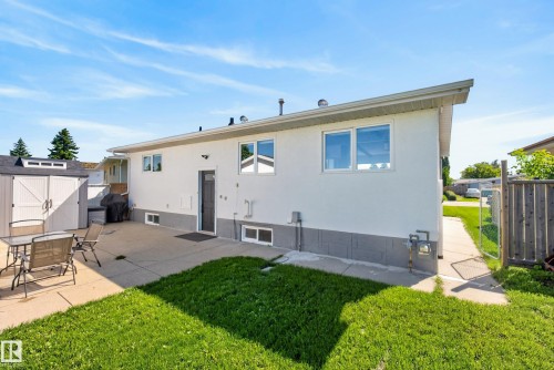 Rear exterior featuring white siding with a gray foundation, a concrete patio, and a dedicated storage shed - 14128 73 Street, Edmonton, AB 
