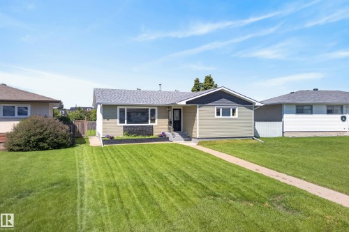 Exterior featuring light green horizontal siding with dark trim accents, a gray shingled roof, a front pathway, and a well-maintained front lawn - 14128 73 Street, Edmonton, AB 
