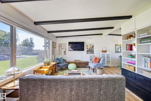 Spacious living area featuring expansive windows, exposed ceiling beams, built-in shelving, and wood-finish flooring - 14128 73 Street, Edmonton, AB 