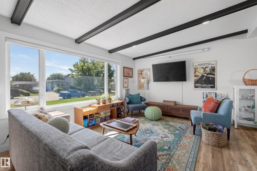 Bright living area featuring a large picture window, exposed ceiling beams with recessed lighting, and wood-finish flooring - 14128 73 Street, Edmonton, AB 