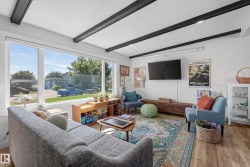 Bright living area featuring a large picture window, exposed ceiling beams with recessed lighting, and wood-finish flooring - 