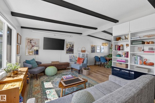 Living area featuring exposed ceiling beams, built-in shelving, wood-finish flooring, and ample natural light from large windows - 14128 73 Street, Edmonton, AB 