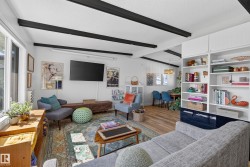 Living area featuring exposed ceiling beams, built-in shelving, wood-finish flooring, and ample natural light from large windows - 