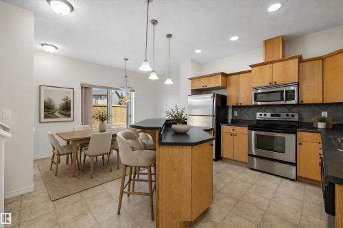 Kitchen and dining area featuring a breakfast bar with pendant lighting, light wood-finish cabinetry, stainless steel appliances, and a tiled backsplash - 101 13825 155 Avenue, Edmonton, AB 