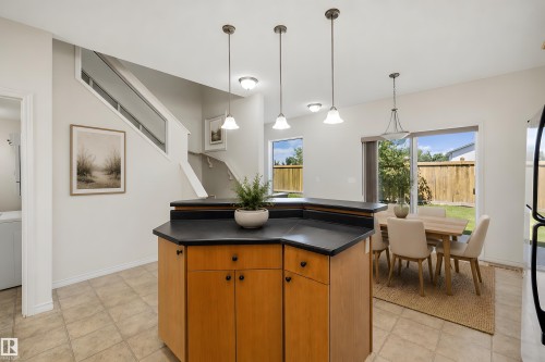 Kitchen island with wood-finish cabinetry, dark countertop, and pendant lighting - 101 13825 155 Avenue, Edmonton, AB 