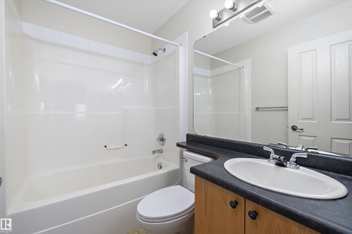 Bathroom featuring a white tub-shower combination, a vanity with a dark countertop and wood-finish cabinetry, and a mirrored wall - 101 13825 155 Avenue, Edmonton, AB 