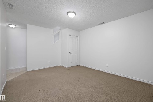Spacious room with neutral carpeting, white walls, and a textured ceiling - 101 13825 155 Avenue, Edmonton, AB 