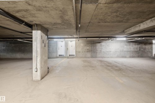 Spacious concrete parking garage featuring overhead lighting, exposed conduit, and multiple access doors - 101 13825 155 Avenue, Edmonton, AB 