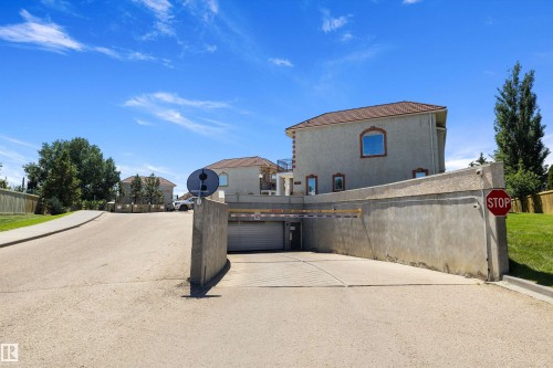 Underground parking entrance featuring a security barrier, concrete retaining walls, and a paved approach - 101 13825 155 Avenue, Edmonton, AB 