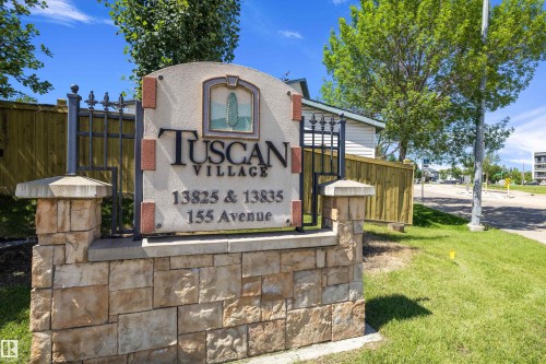 "Tuscan Village" entrance sign featuring a stone base, wrought iron detailing, and an arched stucco panel with a decorative emblem - 101 13825 155 Avenue, Edmonton, AB 