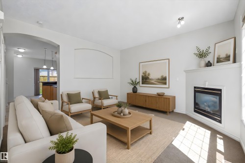 Living room featuring a built-in fireplace with a white mantel, light-colored carpeting, an arched doorway, and recessed ceiling lights - 101 13825 155 Avenue, Edmonton, AB 