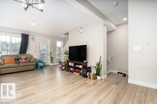 Expansive living area featuring light wood-finish flooring, a contemporary chandelier, recessed ceiling lights, and multiple windows providing natural illumination - 96 1530 Tamarack Boulevard, Edmonton, AB 