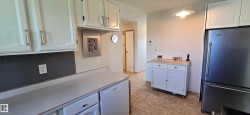 Kitchen featuring white cabinetry with silver-tone hardware, a dark subway tile backsplash, light-toned countertops, and a built-in stainless steel refrigerator - 