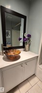 Bathroom vanity featuring a vessel sink with a unique finish, a modern faucet, white cabinetry, a light-toned countertop, and a framed mirror - 