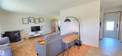 Open concept living area featuring a wood-burning stove on a raised hearth, light wood-finish flooring, and a tiled entryway - 