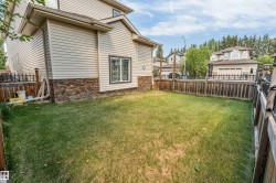 Expansive rear yard featuring green lawn, wood privacy fencing, and a house exterior with horizontal siding and stone veneer detailing - 