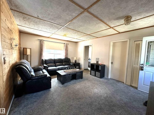 Living area featuring a horizontal wood-paneled accent wall, neutral-toned walls, and grey carpeting - 825 2 Street, Thorhild, AB 