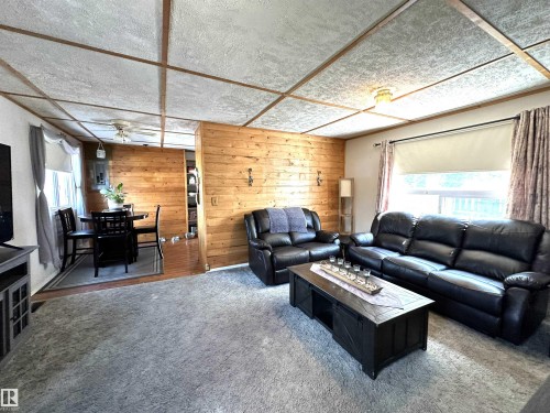 Open-concept living space featuring a wood-panel accent wall, textured ceiling, and light-tone wood-finish flooring in the dining area - 825 2 Street, Thorhild, AB 