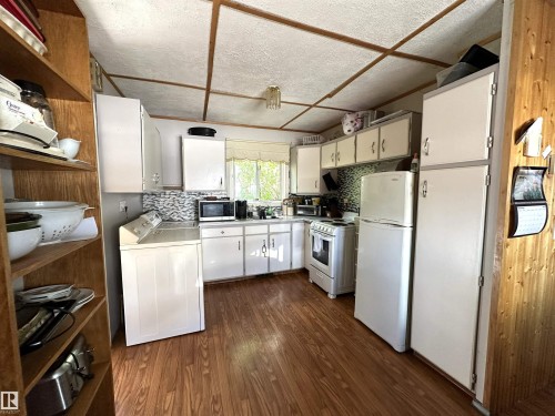 Kitchen featuring wood-finish flooring, white cabinetry, integrated appliances, a tiled backsplash, and a window for natural light - 825 2 Street, Thorhild, AB 