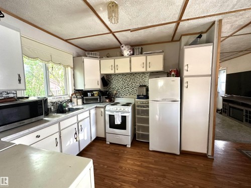 Kitchen featuring wood-finish flooring, white cabinetry, a mosaic tile backsplash, and a window above the sink - 825 2 Street, Thorhild, AB 