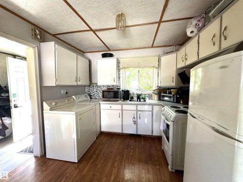 Kitchen space featuring wood-finish flooring, white cabinetry, and a patterned tile backsplash - 825 2 Street, Thorhild, AB 