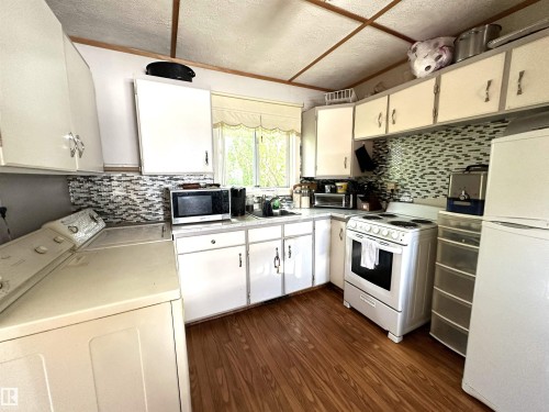 Kitchen featuring wood-finish flooring, white cabinetry, and a mosaic tile backsplash - 825 2 Street, Thorhild, AB 