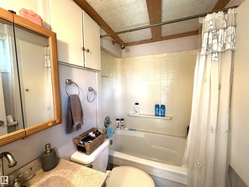 Bathroom featuring a built-in bathtub with tiled surround, a vanity with a counter and sink, an overhead mirror, and built-in upper cabinetry - 825 2 Street, Thorhild, AB 