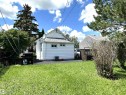 Expansive grassy yard area with mature trees and shrubbery framing the property - 825 2 Street, Thorhild, AB 