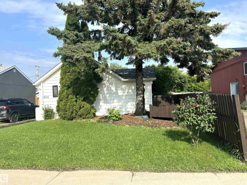 Front exterior featuring white siding, a prominent evergreen tree, and a dark wood fence - 825 2 Street, Thorhild, AB 