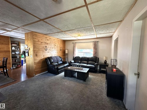Living area featuring wood-paneled walls and a textured ceiling with wood trim - 825 2 Street, Thorhild, AB 