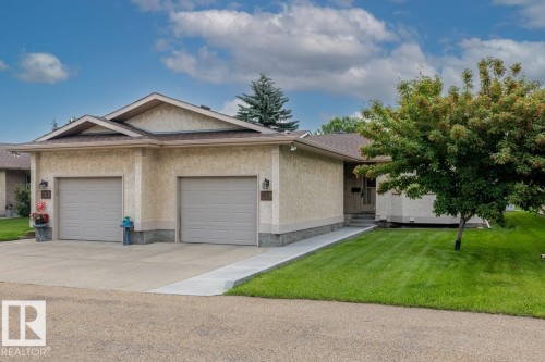 Stucco exterior with stone accenting, featuring a dual-bay garage with individual doors, a concrete driveway, and a well-maintained lawn - 219 Knottwood Road, Edmonton, AB 