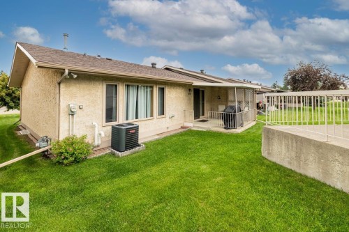 Stucco exterior featuring a covered patio, shingle roofing, and a well-maintained lawn - 219 Knottwood Road, Edmonton, AB 