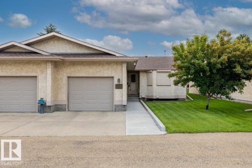 Stucco exterior featuring dual garage doors, a concrete driveway, and a front entry ramp - 219 Knottwood Road, Edmonton, AB 