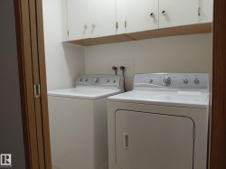 Dedicated laundry area featuring white upper cabinetry with brass hardware and a built-in shelf - 