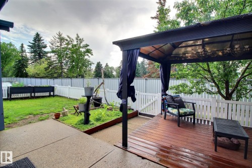 Outdoor living space featuring a covered wooden deck, privacy curtains, and a white picket fence - 30 14620 26 Street, Edmonton, AB 